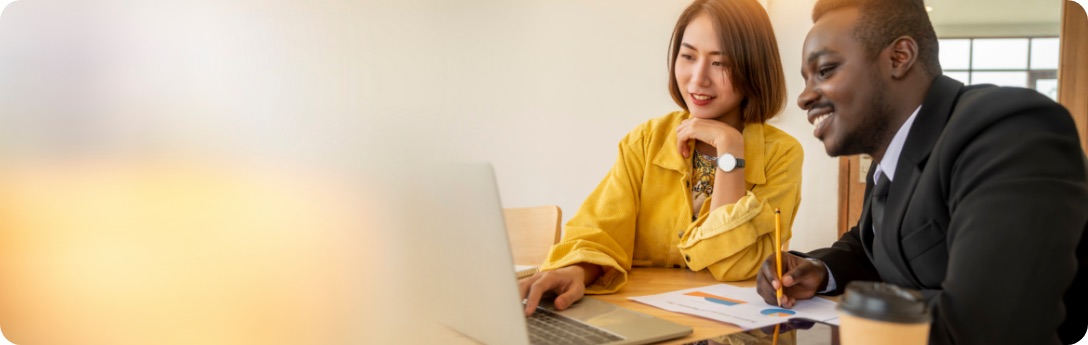 Woman and man sitting at desk while writing and looking at laptop