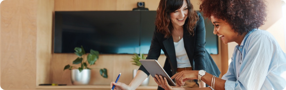 Two women in office looking at tablet while smiling